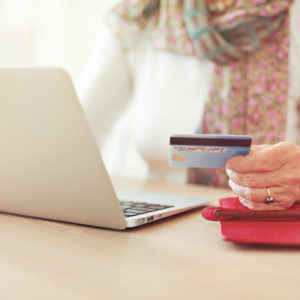 Senior woman's hand holding a credit card while in front of the laptop shopping online